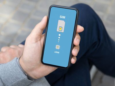 Mężczyzna trzyma w dłoni smartfon, na którego ekranie widać ustawienia SIM i eSIM na niebieskim tle.
