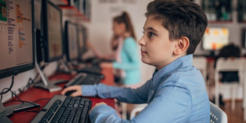 Młody chłopiec wykorzystuje komputer dla ucznia do nauki w sali szkolnej.