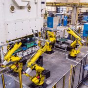 Cztery roboty przemysłowe współpracują na hali produkcyjnej na jednym stanowisku.