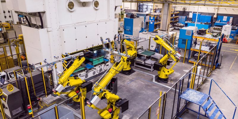 Cztery roboty przemysłowe współpracują na hali produkcyjnej na jednym stanowisku.
