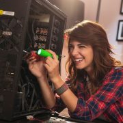 Młoda kobieta w koszuli w kratkę przeprowadza samodzielne składanie komputera przy wykorzystaniu śrubokrętów.