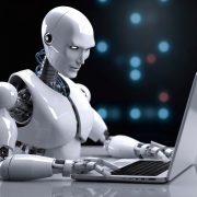 Czy sztuczna inteligencja zastąpi programistów? Na zdjeciu robot w roli programisty przed laptopem.